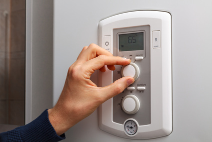 Men hand regulate temperature on 65 degree in control panel of central heating.